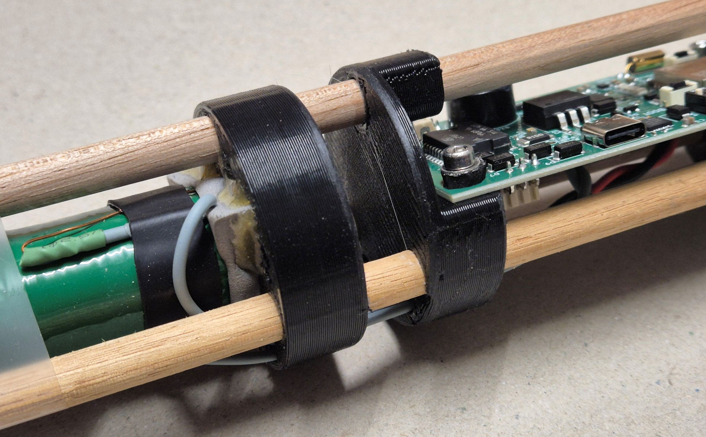 Assembly showing 3D-printed support discs, wooden dowels supporting the ferrite core rods, and 18650 lithium-ion battery pack.